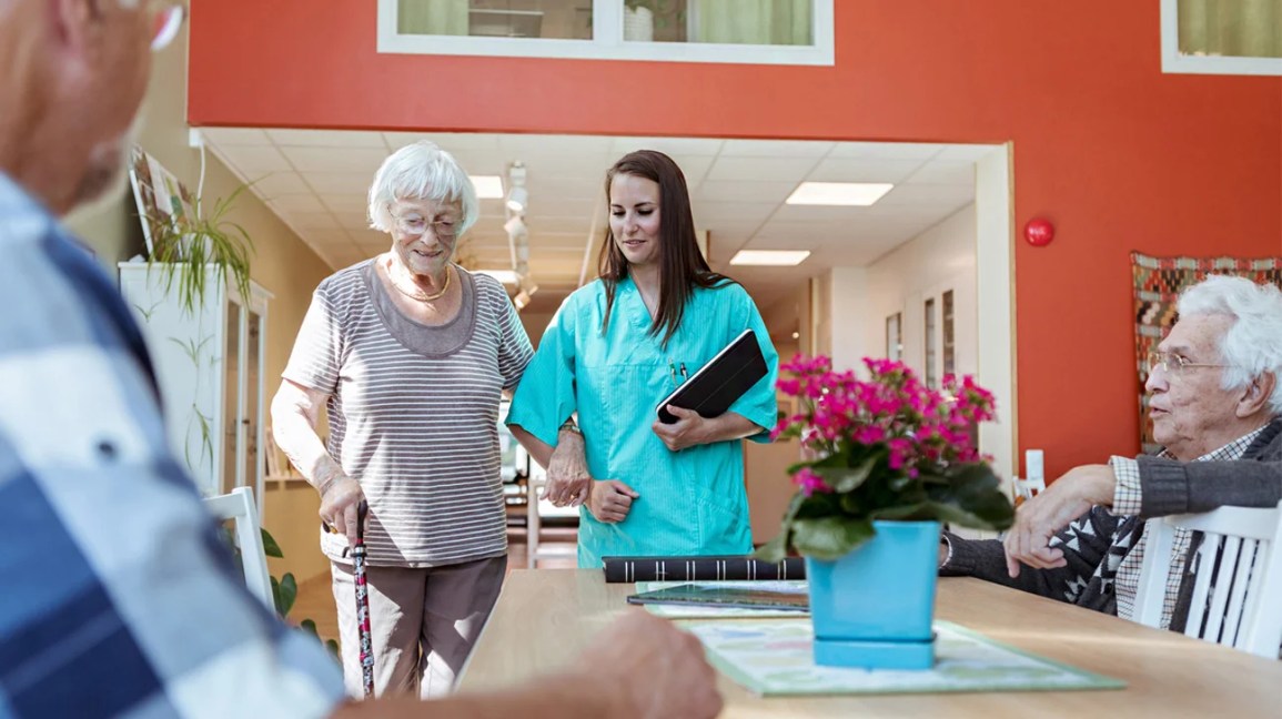 older woman walking with an aide in a skilled nursing facility-1